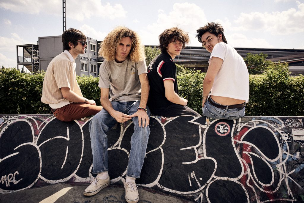 EN: Liily band members sitting on a graffiti-covered ledge at a Berlin skatepark, exuding punk rock style. Photo by Bert. DE: Liily sitzt auf einer mit Graffiti bedeckten Kante im Berliner Skatepark – mit deutlichem Punkrock-Stil. Fotografiert von Bert.