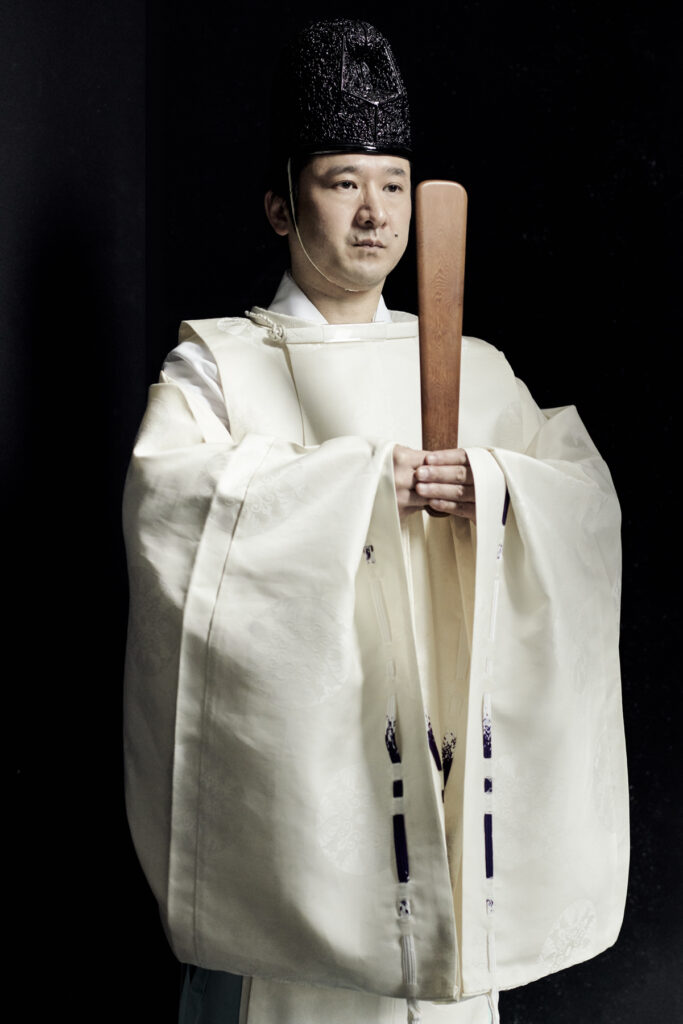 Formal portrait of Shinto priest Masatsugu Okutani holding ritual baton in ceremonial robe, photographed by Bert Spangemacher