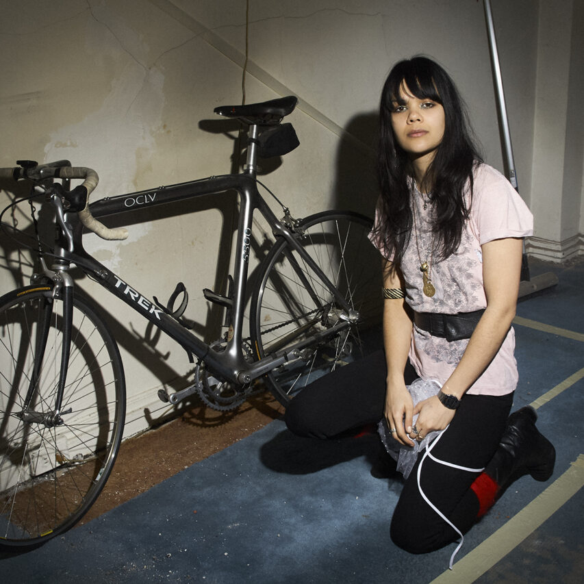 Natasha Khan of Bat for Lashes kneeling beside a vintage TREK bicycle, photographed by Bert Spangemacher in New York City